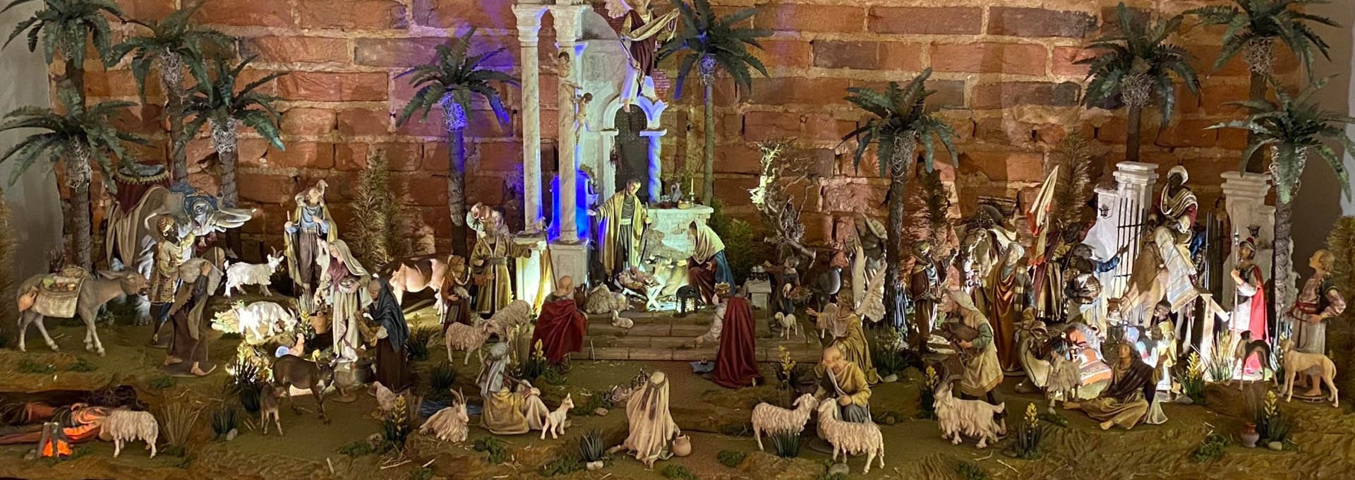 A sprawling nativity village of carved figures, palm trees and stone ruins set against a brick wall.