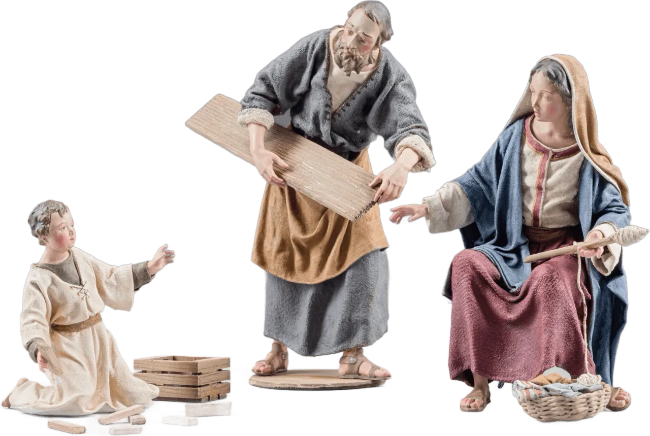 Hand-carved wooden nativity figures of Boy Jesus kneeling, Joseph holding wood plank, and Mary seated with spindle, dressed in fabric